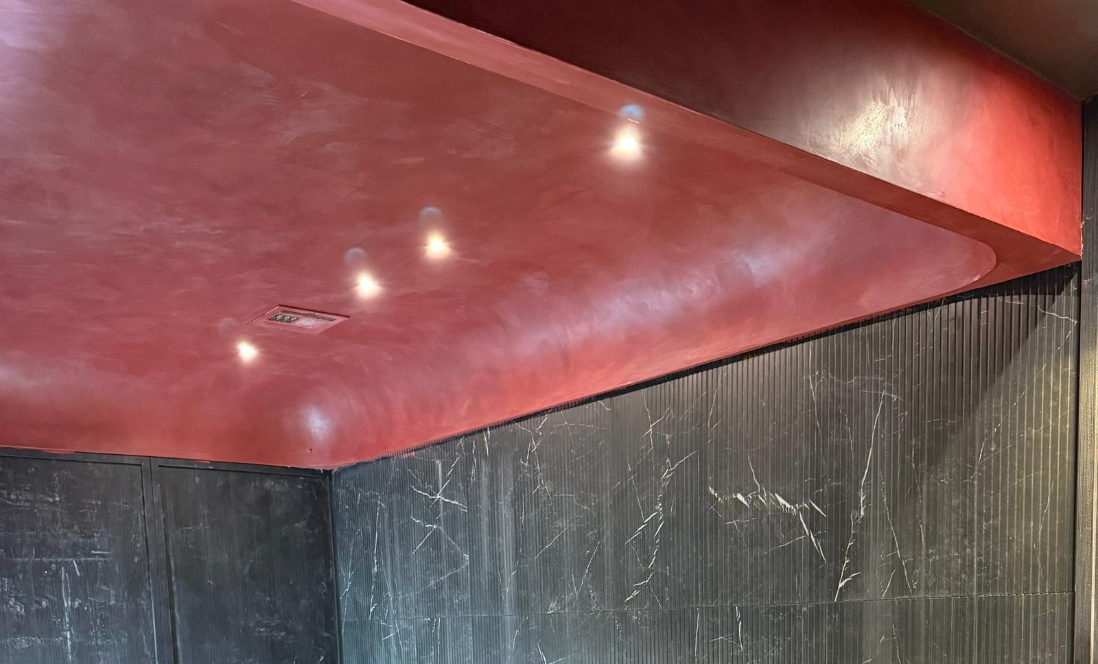 Claret oxblood Venetian plaster ceiling cove, burnished to a metallic sheen, meeting book-matched Pietra Grey marble walls in a dark Brooklyn interior — MarkOn® Walls / Vlad Markov