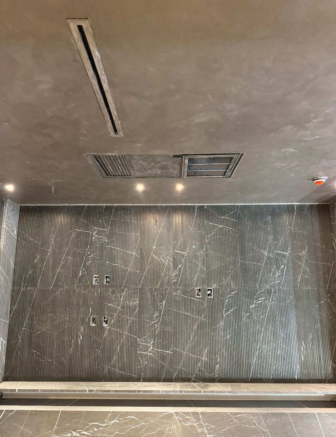 Liquid-graphite metallic polished plaster ceiling with a linear diffuser, above a fluted and book-matched Pietra Grey marble feature wall — MarkOn® Walls / Vlad Markov, Brooklyn