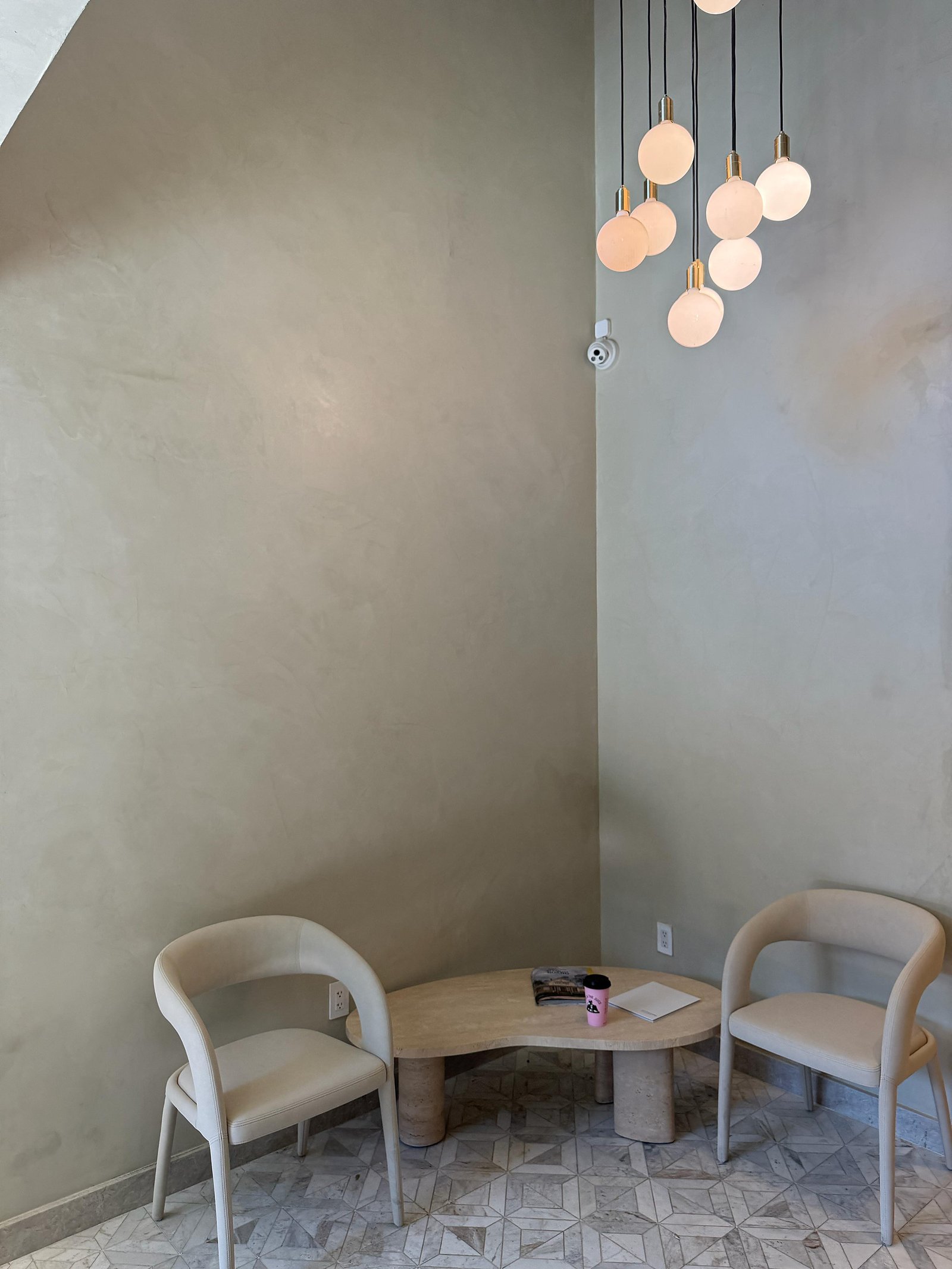 Double-height residential lobby in warm hand-troweled lime plaster, alabaster pendant cluster, travertine table and cream chairs on a marble-mosaic floor — MarkOn® Walls