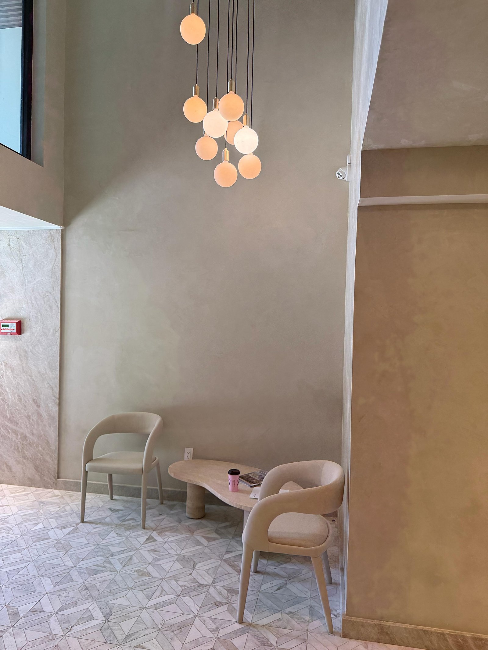 Lobby seating vignette — warm lime-plaster walls, microcement column, alabaster pendants and travertine table — MarkOn® Walls