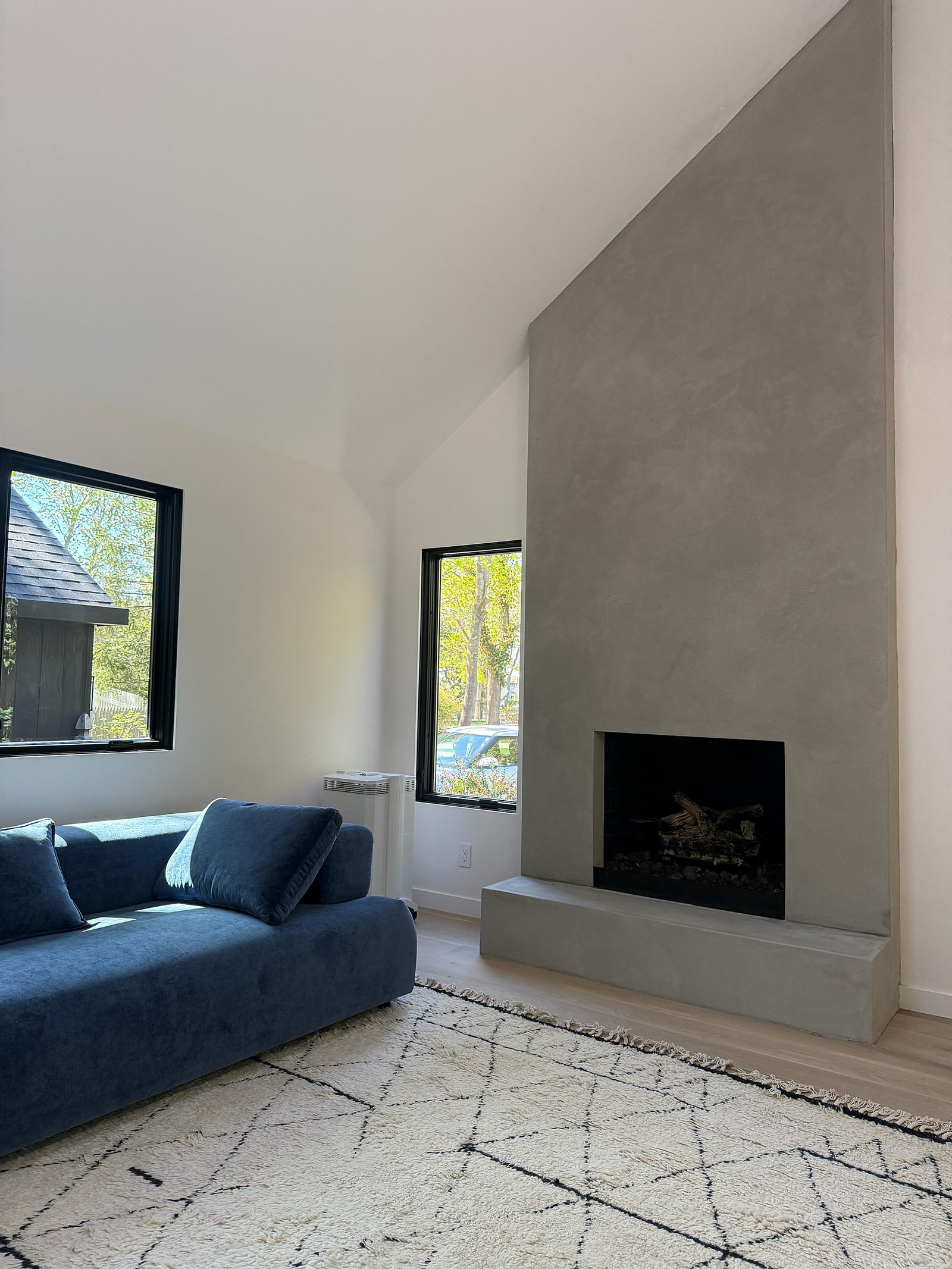 Vaulted Montauk living room with a full-height microcement chimney breast in soft coastal grey, blue sofa and Moroccan rug — MarkOn® Walls