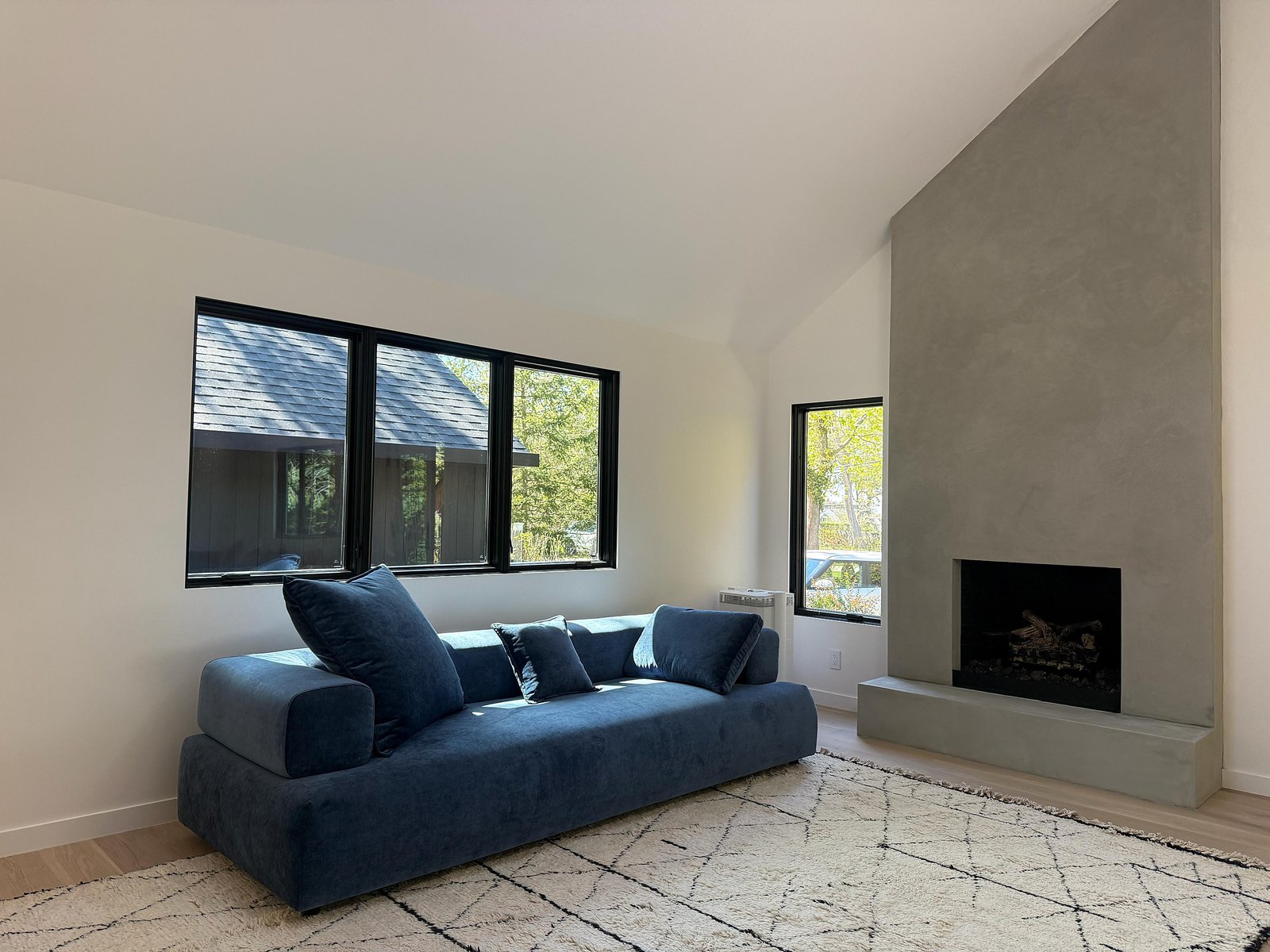 Montauk living room with microcement fireplace, blue sofa, black-framed windows and a geometric rug — MarkOn® Walls